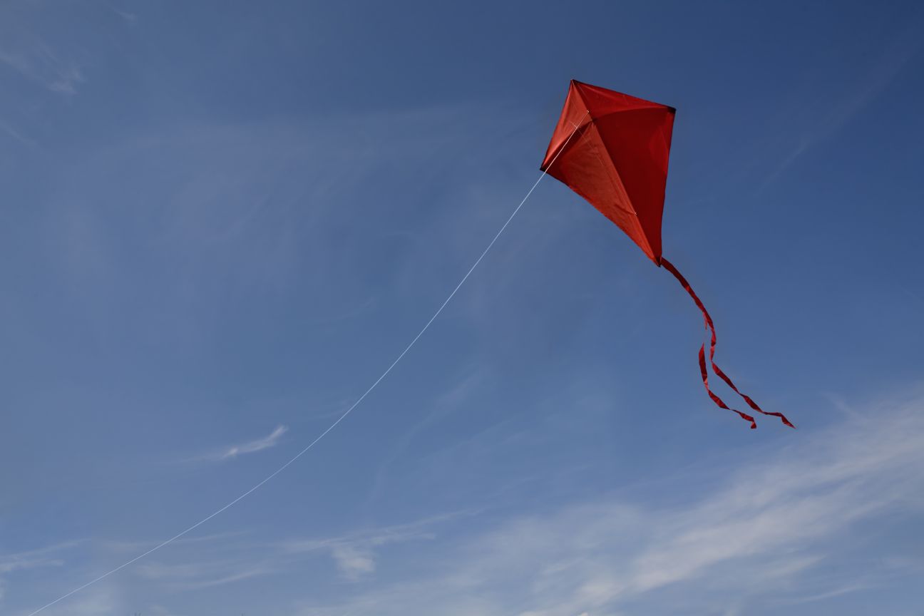A red kite with a string flying against a blue sky.