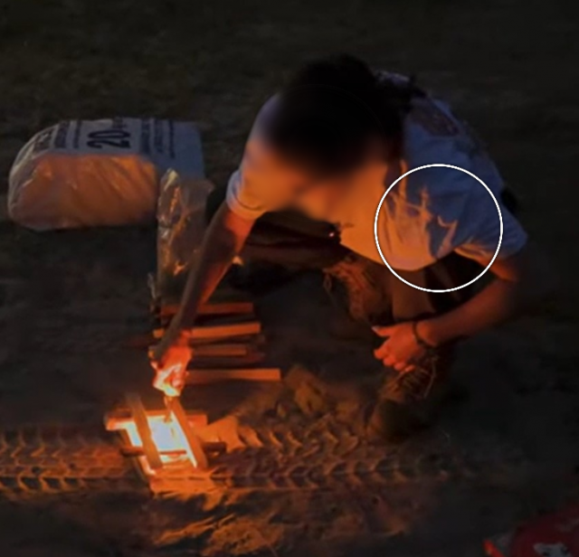 A person sits beside a fire, their face is blurred