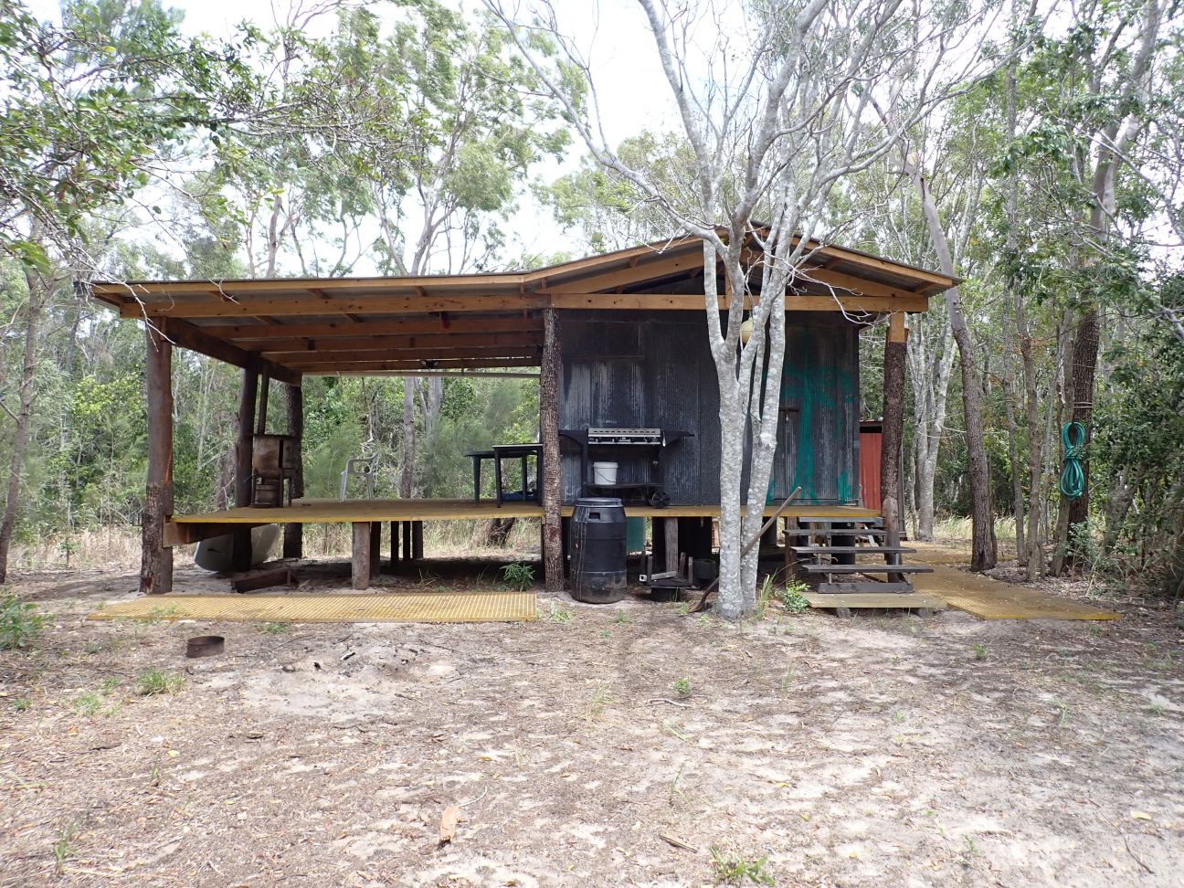 A small wooden cabin nestled in the woods, featuring a grill on the porch for outdoor cooking.  