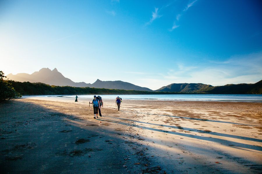 Four people walking across a vast expanse of sandy beach with mountains in the background.