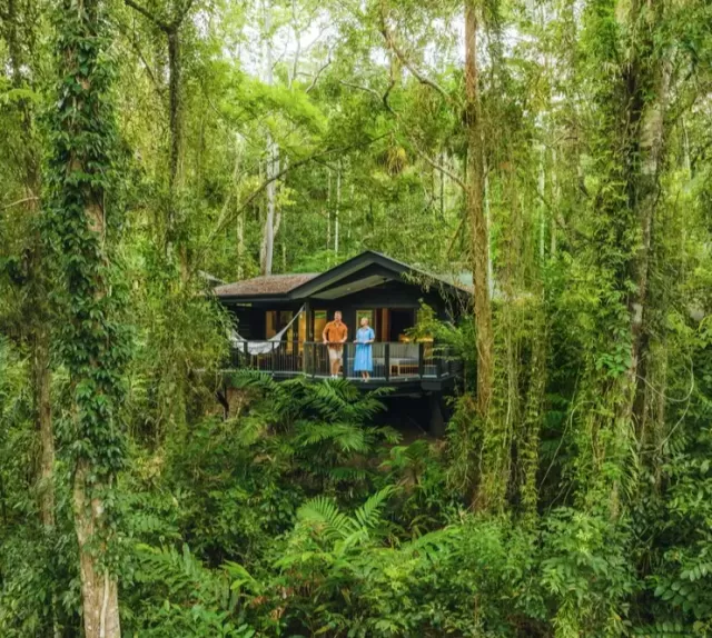 Photo of a man and a woman on the balcony of a cabin surrounded by rainforest