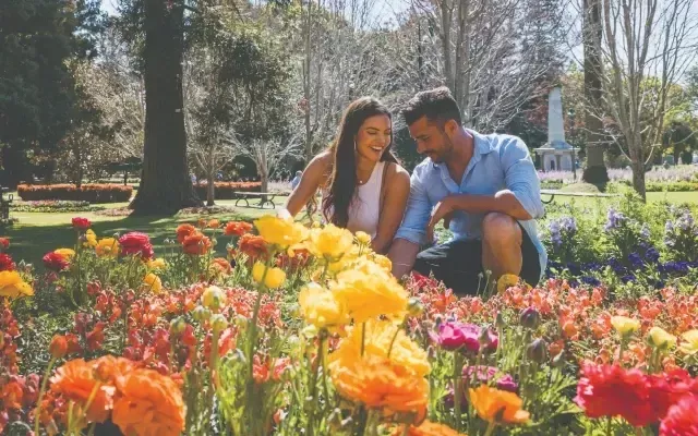 Photo of a man and women sitting in a park beside a flowering garden