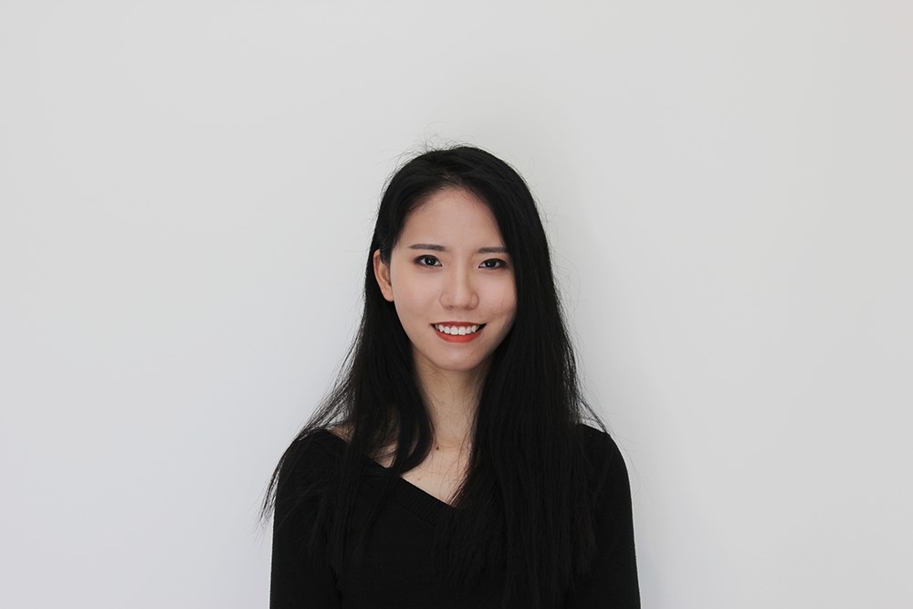 A headshot of a woman with long black hair, red lipstick, and a black shirt standing against a white background.