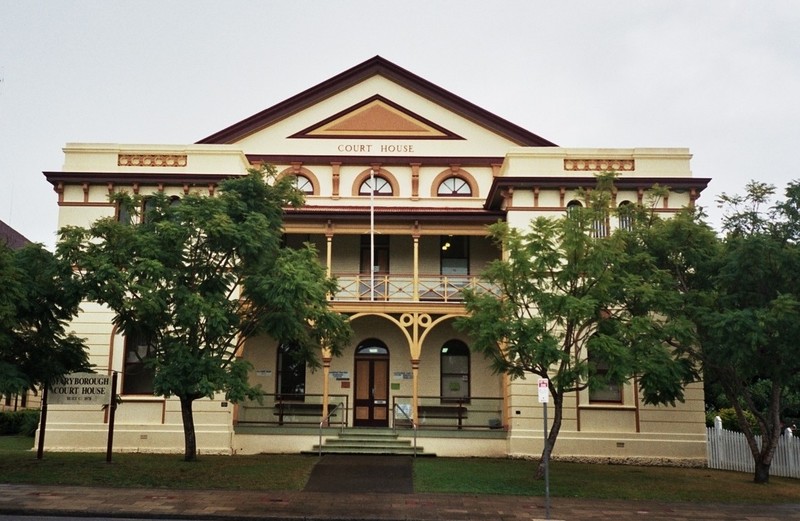 A large two-storey cream building with tall green trees on either side.