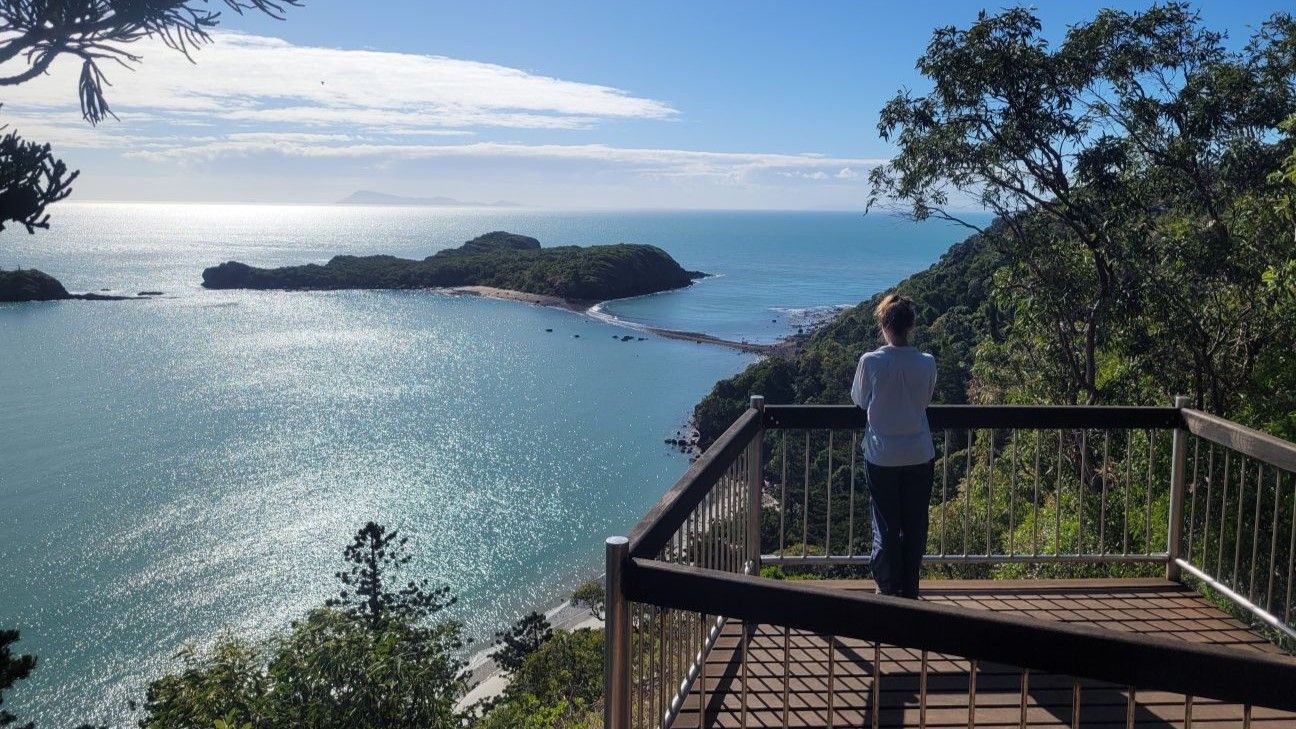 Rear vision of a person on a raised wooden lookout platform. They are observing an ocean scene with an island visible in the foreground.
