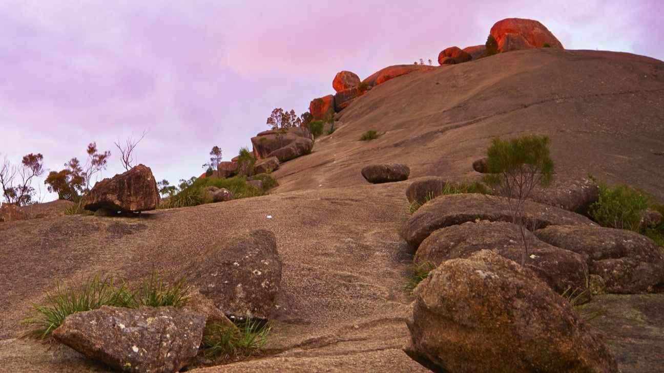 A steep mountain face dotted with large boulders and sparse greenery.