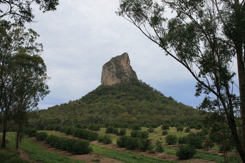 A large peak of grey-brown volcanic rock juts out amongst greenery on a steep slope.